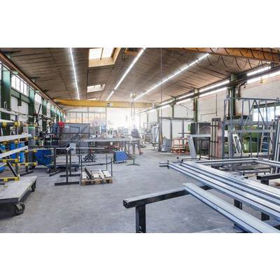 Große Industriehalle mit Metallgerüsten und Maschinen. Eine Person im Hintergrund arbeitet in der gut beleuchteten Werkstatt.