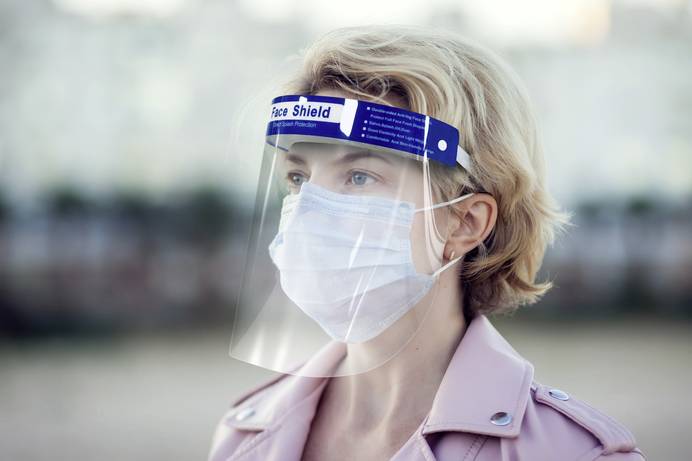 Eine Person mit freiem Schutzvisier und Atemmaske schaut in die Ferne.