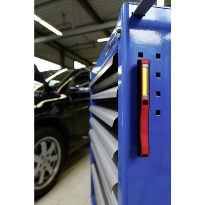Blauer Werkstattwagen mit Werkzeug, rotes Magnetlicht befestigt. Im Hintergrund steht ein Auto mit geöffneter Motorhaube in einer Werkstatt.