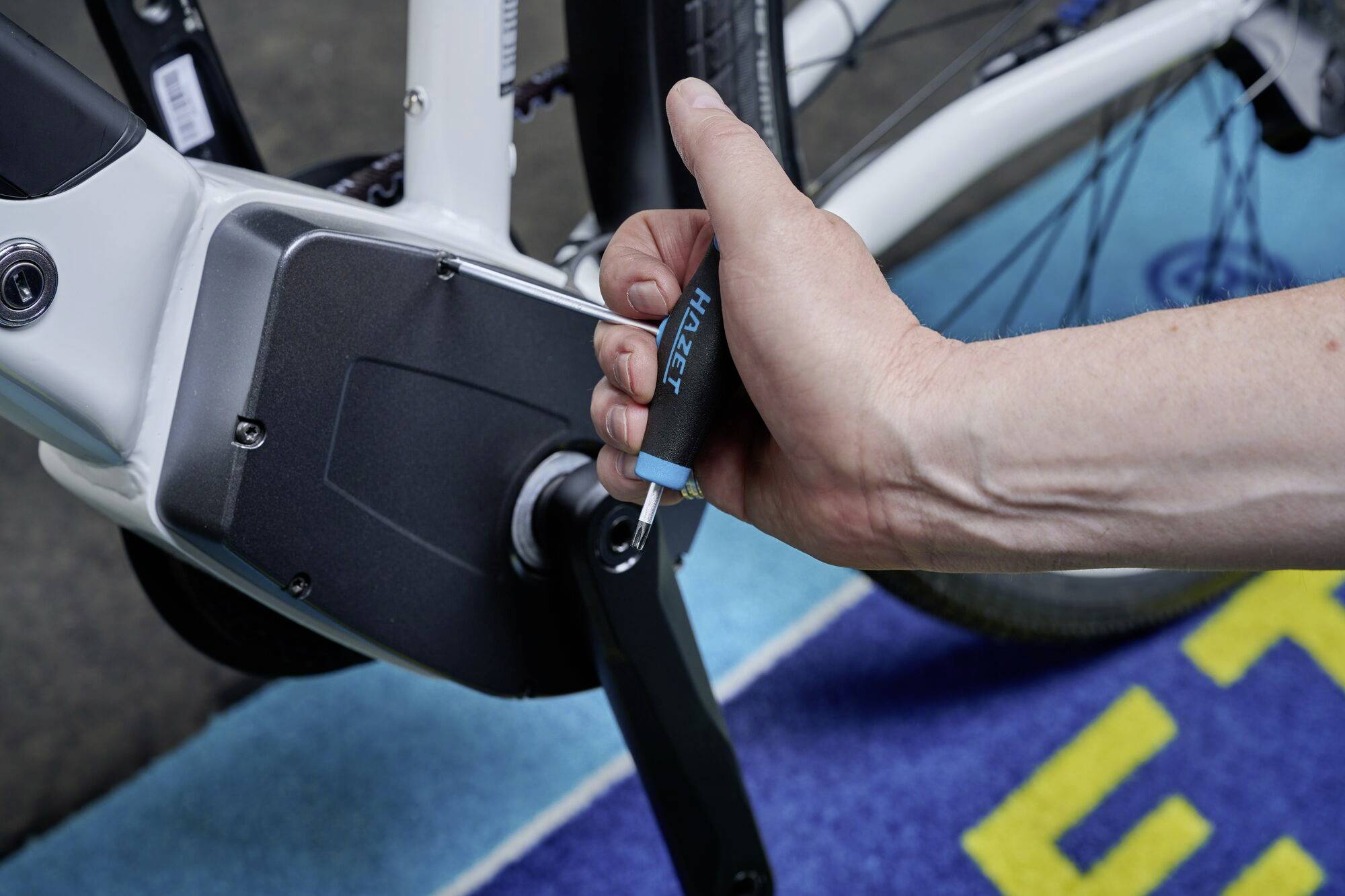 Eine Hand verwendet ein Werkzeug, um die Pedale eines weißen Fahrrads zu montieren oder anzupassen. Fokus auf dem Montageprozess.