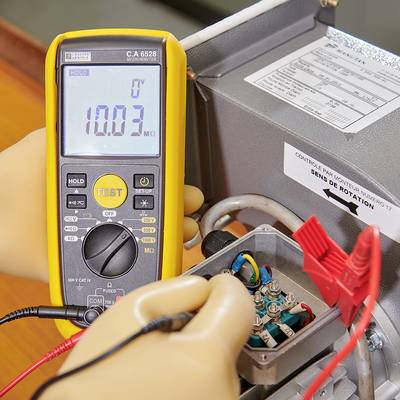 Ein Multimeter zeigt '10,03 MΩ', gehalten von einer Person mit Handschuhen, misst eine elektrische Schaltung in einem Metallgehäuse.