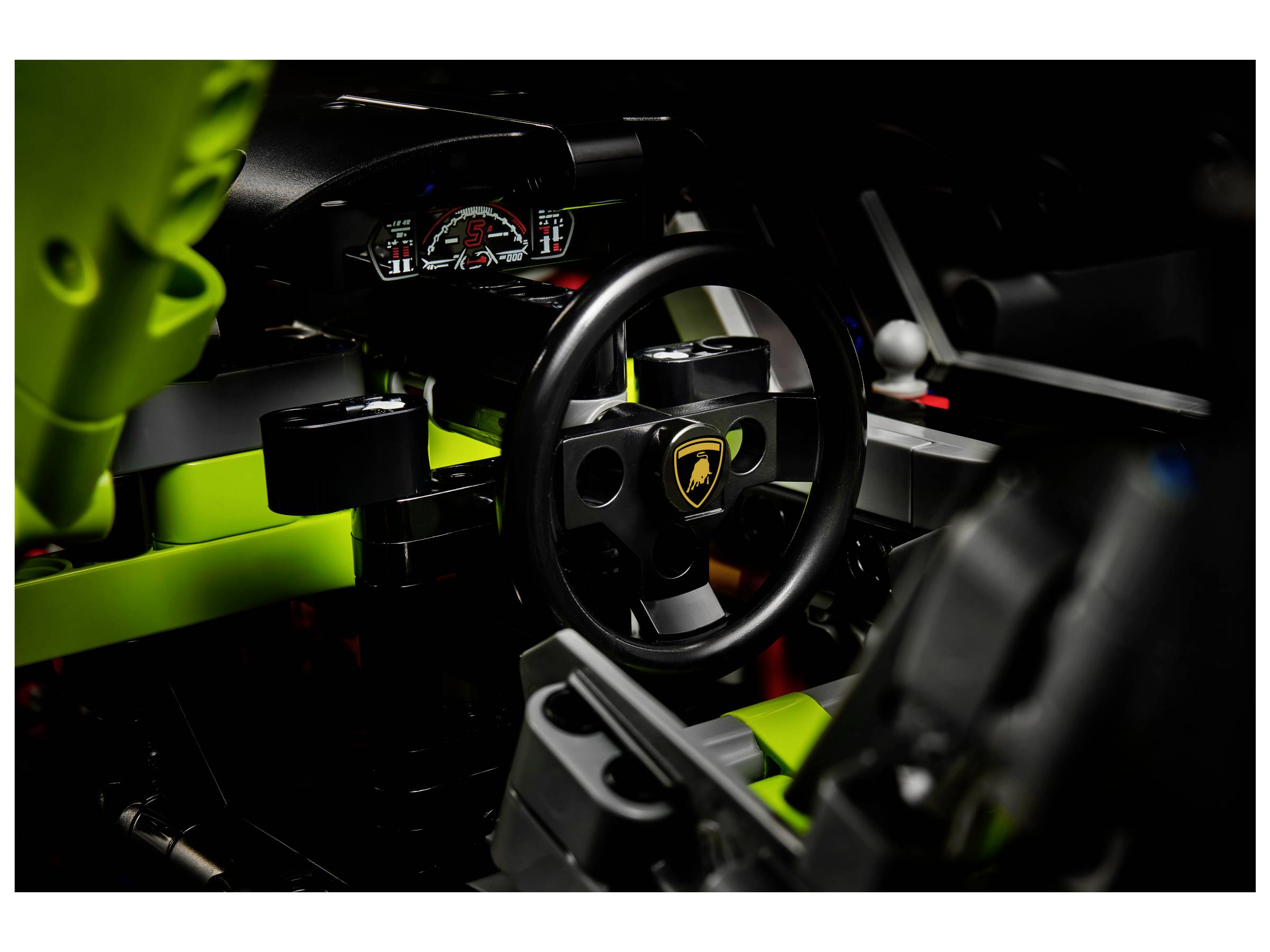 Innenansicht eines Spielzeug-Sportwagenmodells mit Lenkrad und Armaturenbrett. Das Lenkrad zeigt ein gelbes Markenlogo.