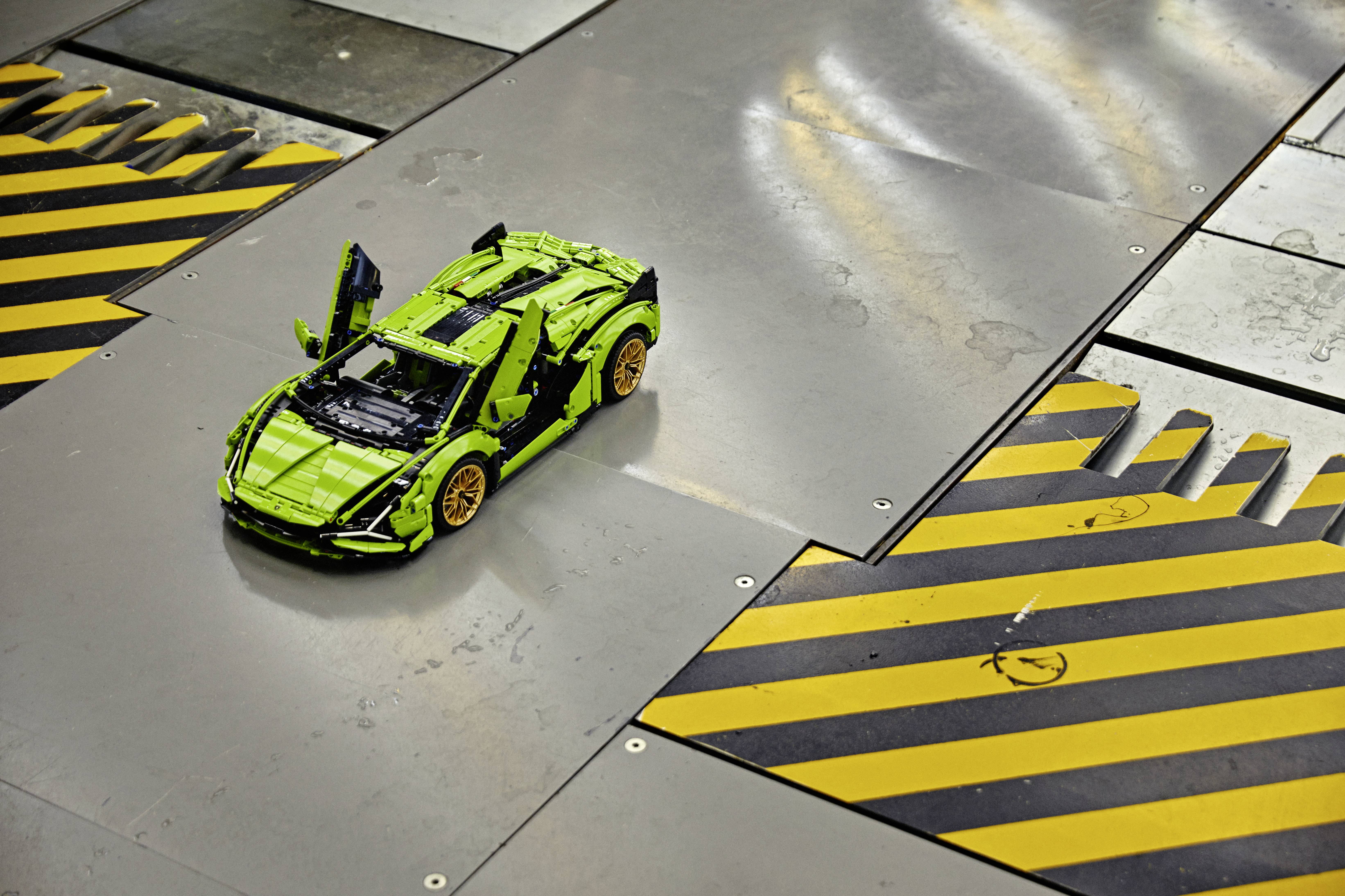 Spielzeugauto aus Bausteinen in Limousinen-Design, grün mit goldenen Felgen, steht auf einem silbernen Boden mit gelben und schwarzen Streifen.