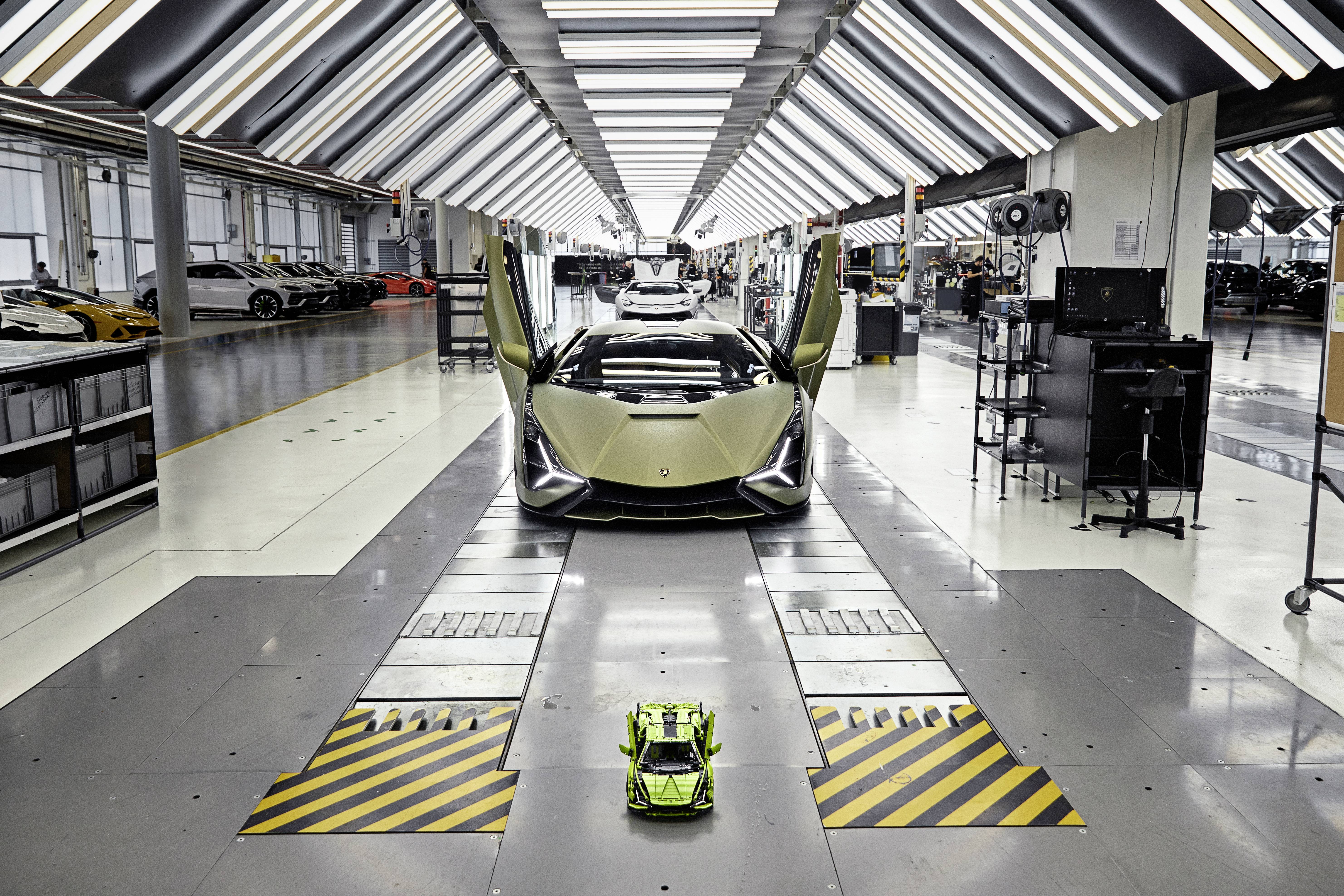 Ein olivgrünes Auto mit geöffneten Flügeltüren steht in einer Produktionshalle. Im Vordergrund steht ein kleines Modellauto.