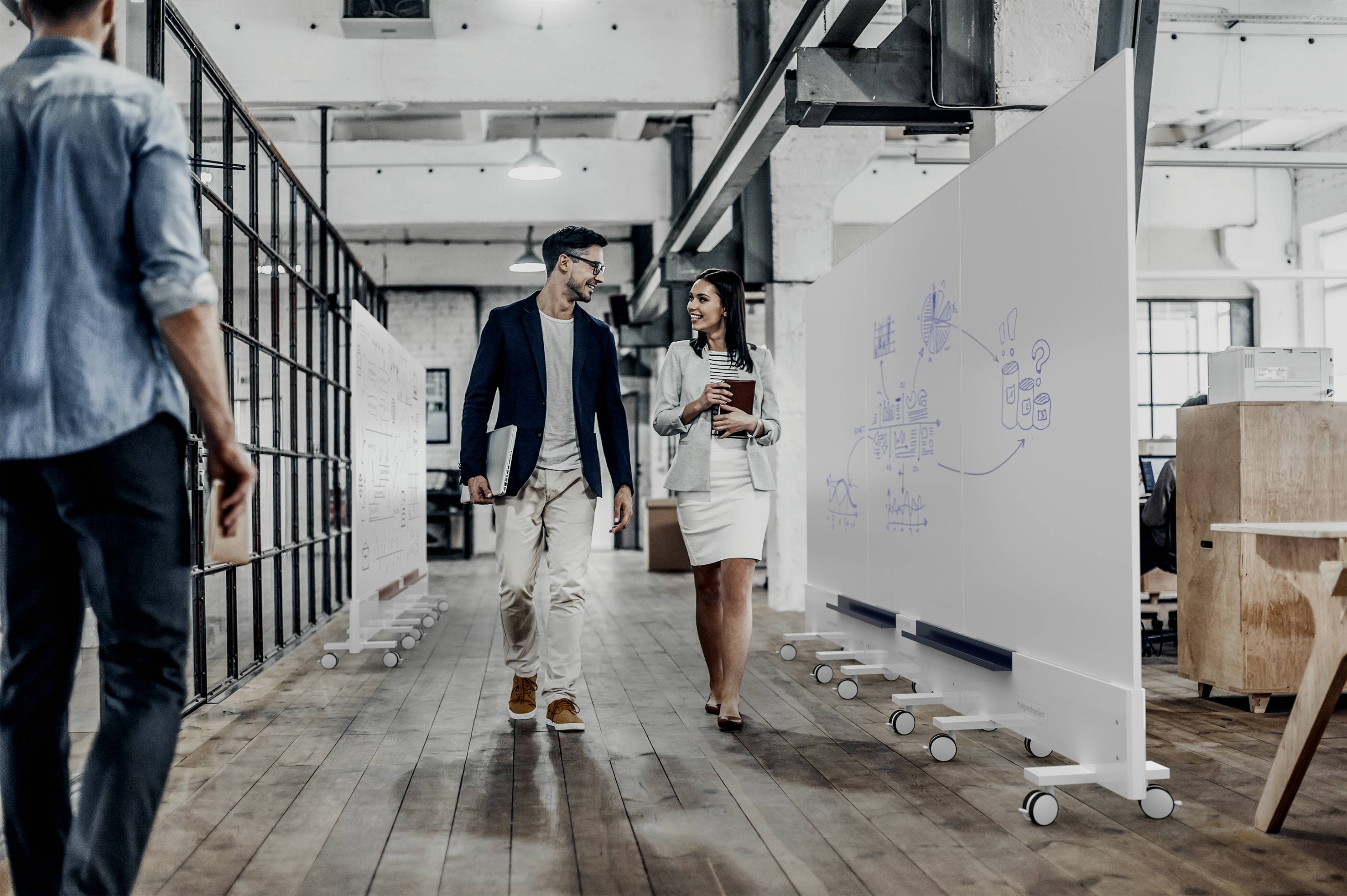 Ein Mann und eine Frau gehen und unterhalten sich in einem modernen Büro mit Whiteboards im Hintergrund.