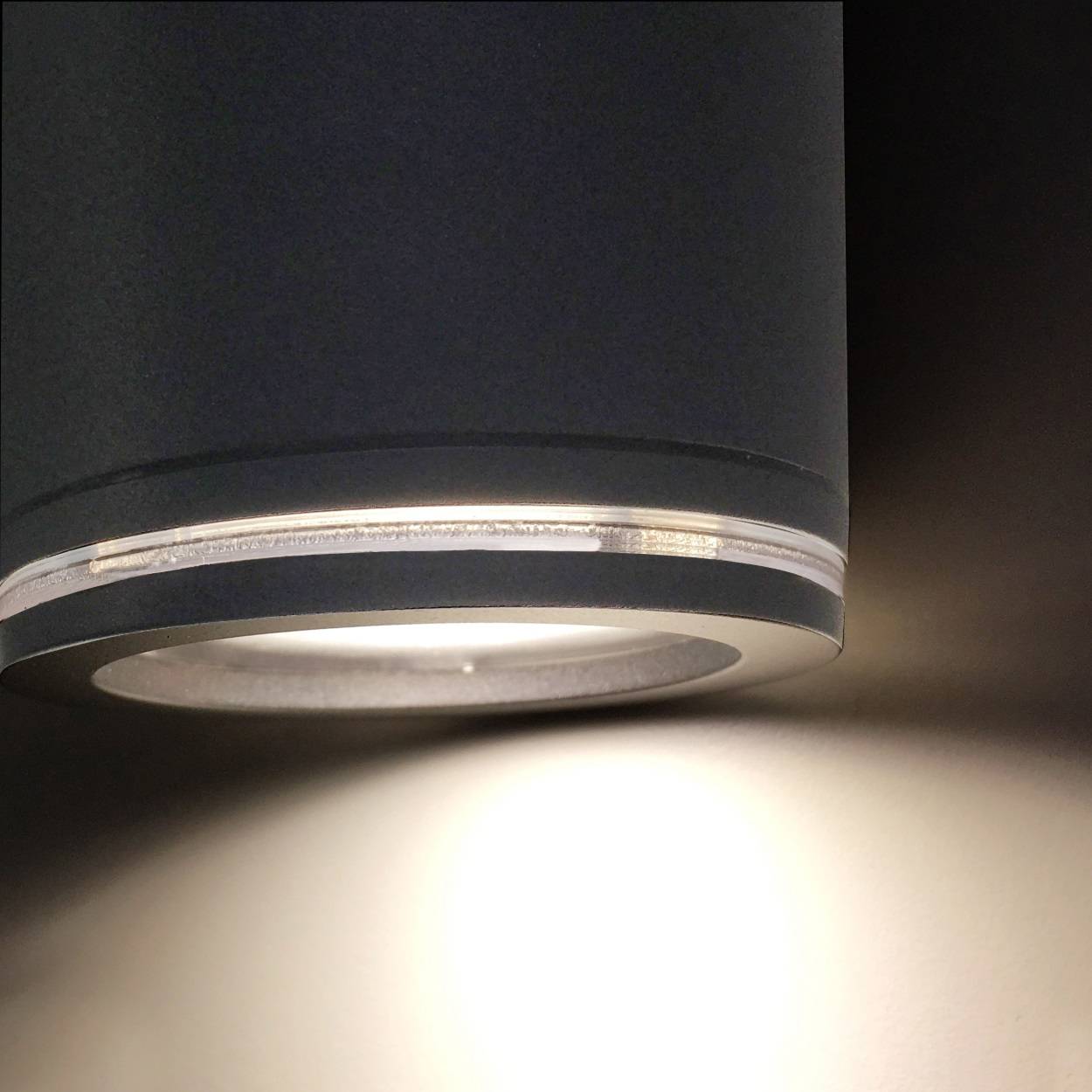 Eine moderne, zylindrische Wandlampe, die weiches Licht auf eine helle Wand abstrahlt.