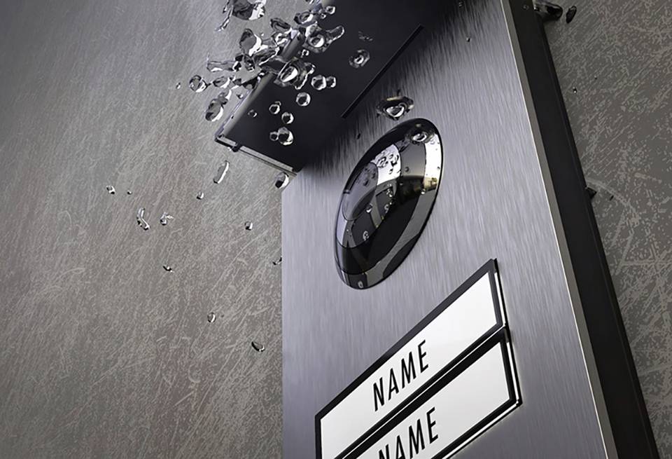 Türschild mit kaputter Kamera und herausgefallenen Glasscherben. Zwei Namensfelder darunter leer.