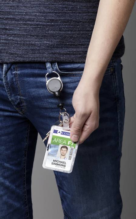 Eine Person trägt eine blaue Jeans und hält einen Ausweis mit einem Clip in der Hand. Der Ausweis zeigt ein Foto und den Namen 'Michael Simmons'.