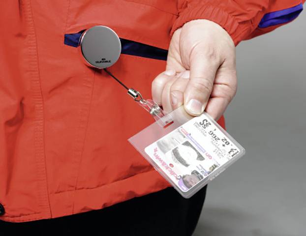 Eine Hand hält ein Namensschild an einem ausziehbaren Schlüsselband, das an einer roten Jacke befestigt ist.