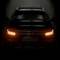 Ein schwarzes Auto mit leuchtenden Frontscheinwerfern, das frontal im Dunkeln gezeigt wird. Auf dem Nummernschild steht 'OSRAM'.