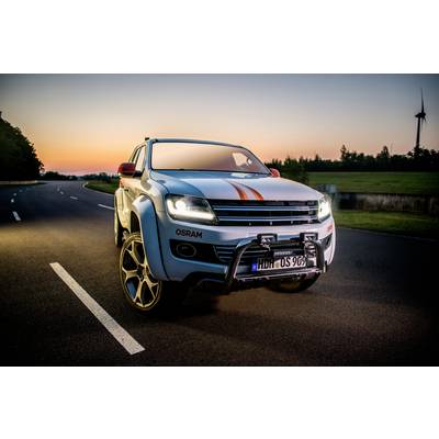 Ein weißer SUV mit orangen Streifen steht auf einer Straße bei Sonnenuntergang. Ein Windrad ist im Hintergrund zu sehen.