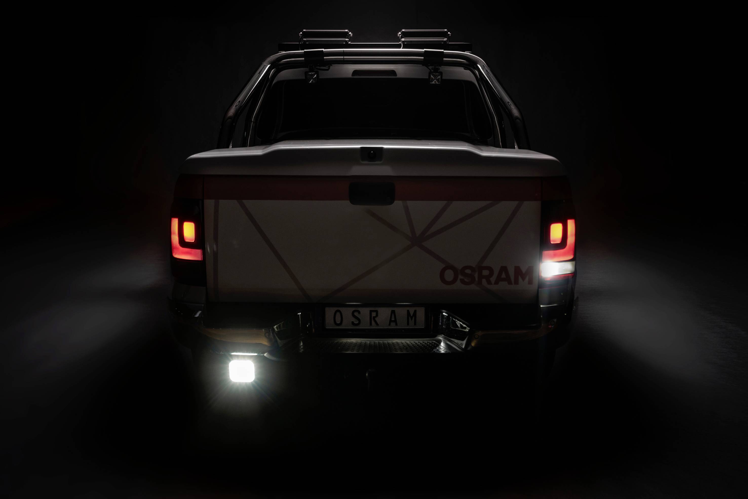 Ein Fahrzeug mit leuchtenden Rücklichtern und einem Nummernschild mit der Aufschrift 'OSRAM', steht in dunkler Umgebung.