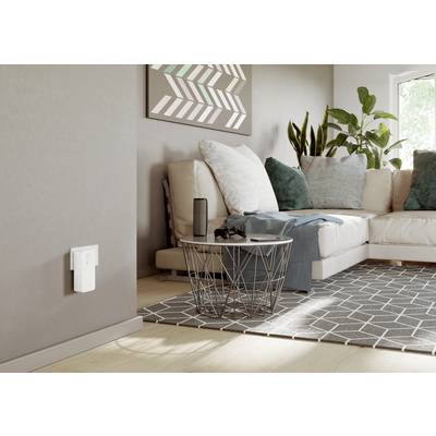 Ein modernes Wohnzimmer mit einem Sofa, Zierkissen, Pflanzen und einem Couchtisch auf einem geometrischen Teppich. Ein Lautsprecher steht auf dem Tisch.