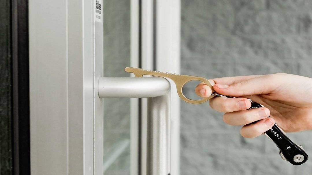 Hand nutzt ein türöffnendes Werkzeug, um einen Türgriff zu betätigen, ohne ihn direkt zu berühren.
