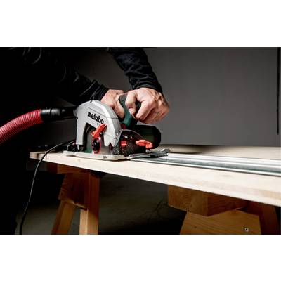 Eine Person benutzt eine Handkreissäge, um ein Holzbrett zu schneiden. Die Umgebung ist eine Werkstatt mit gedämpfter Beleuchtung.