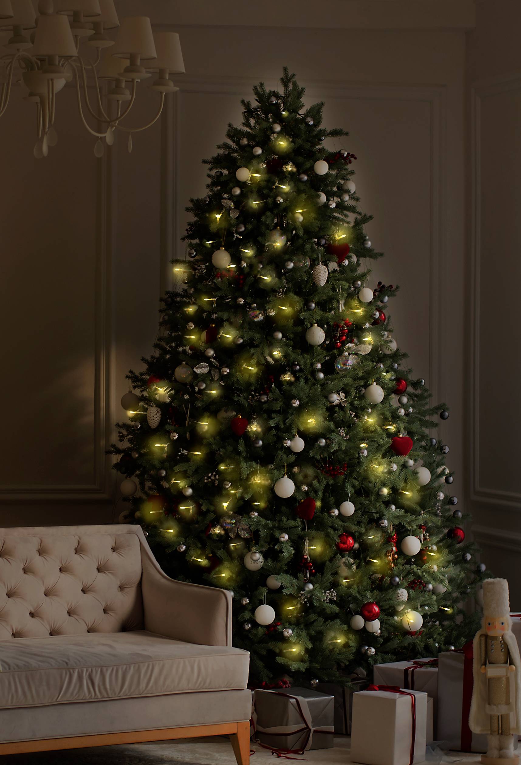 Ein geschmückter Weihnachtsbaum steht in einem Wohnzimmer. Er ist mit roten und weißen Kugeln sowie Lichtern dekoriert, Geschenke liegen darunter.