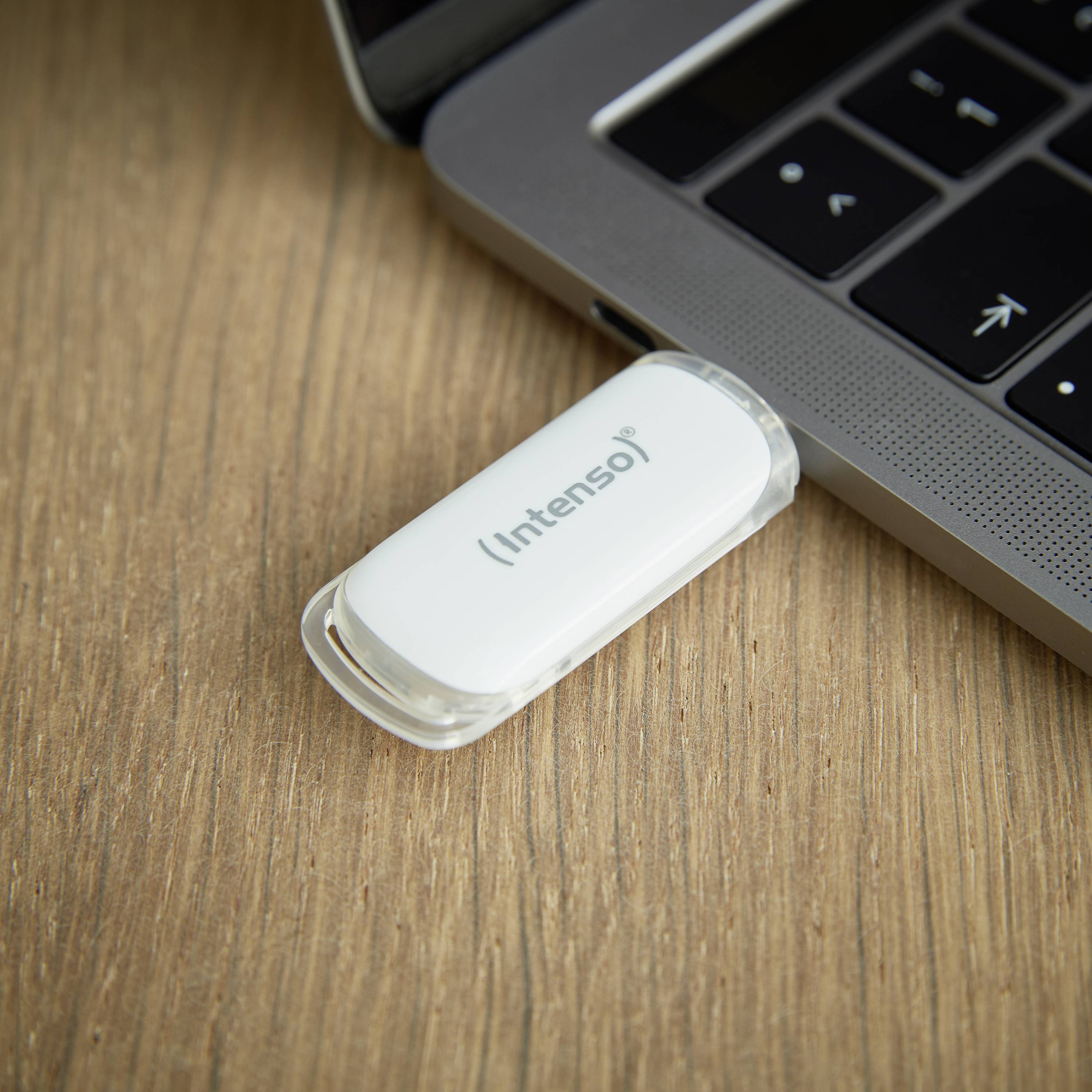 Ein weißer USB-Stick der Marke Intenso steckt in einem Laptop.