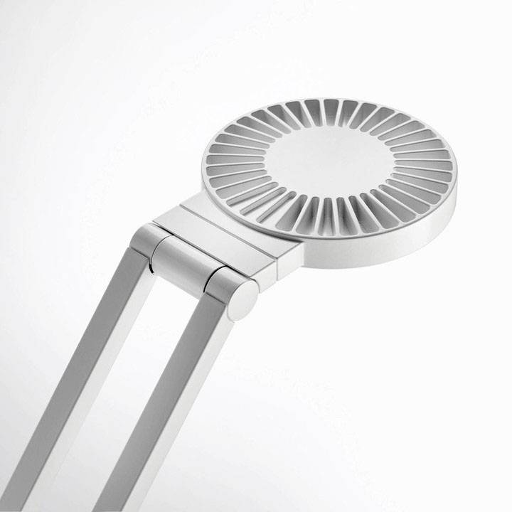 Eine moderne, silberfarbene Schreibtischlampe mit rundem, scheibenförmigem Kopf und Gelenkarm, auf einem neutralen Hintergrund.