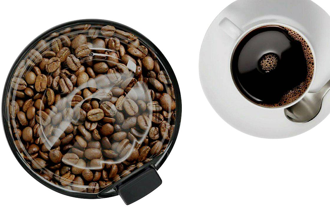 Kaffeebohnen in einem runden Behälter neben einer gefüllten Tasse Kaffee auf weißem Hintergrund.