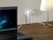 Laptoptisch mit Lampe und Steckdose an der Wand, in der ein Ladegerät eingesteckt ist. Laptopschirm zeigt Weltallmotiv.