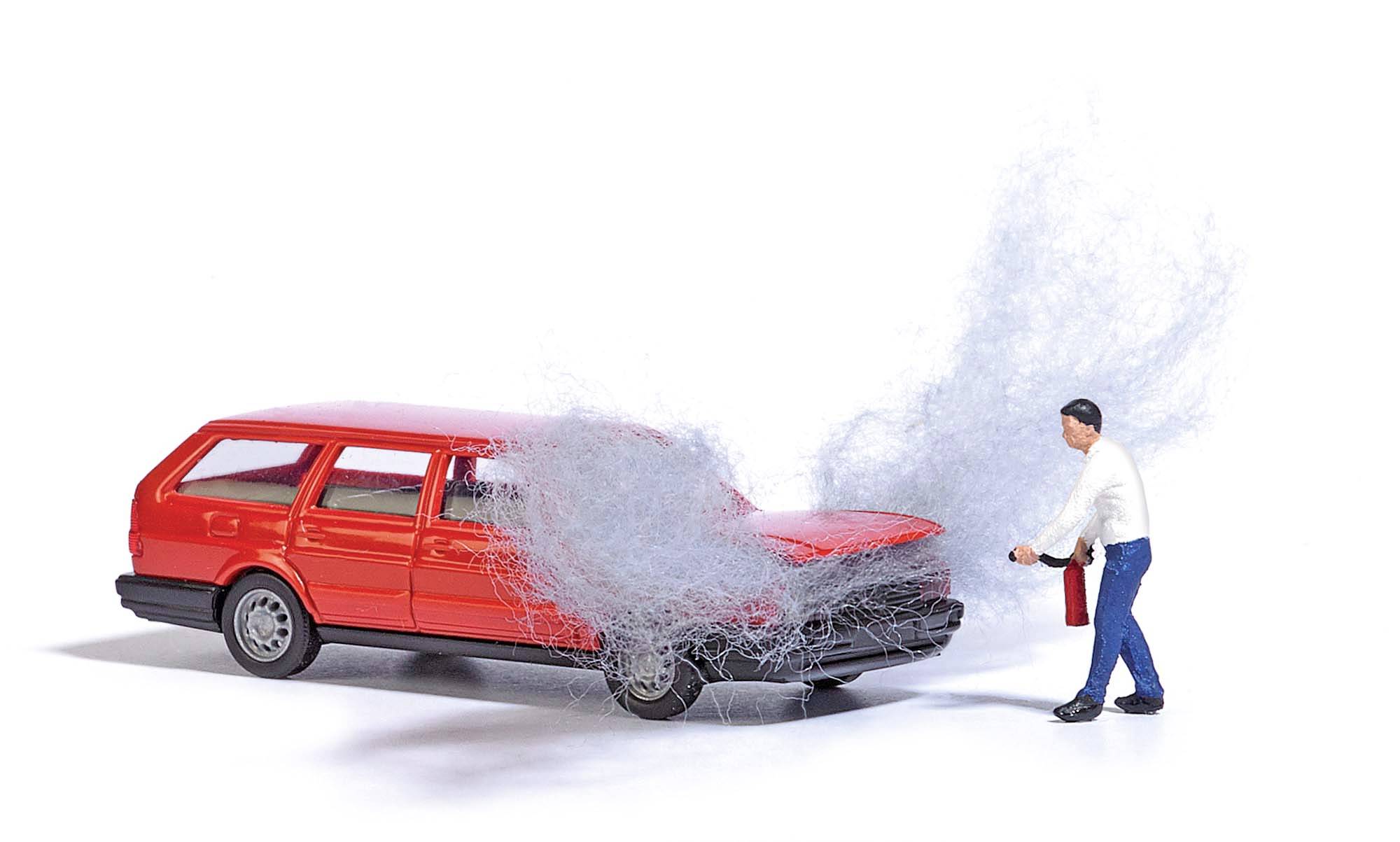 Ein Mann hält einen Feuerlöscher und sprüht Schaum auf die Motorhaube eines roten Kombis, aus dem Rauch aufsteigt.