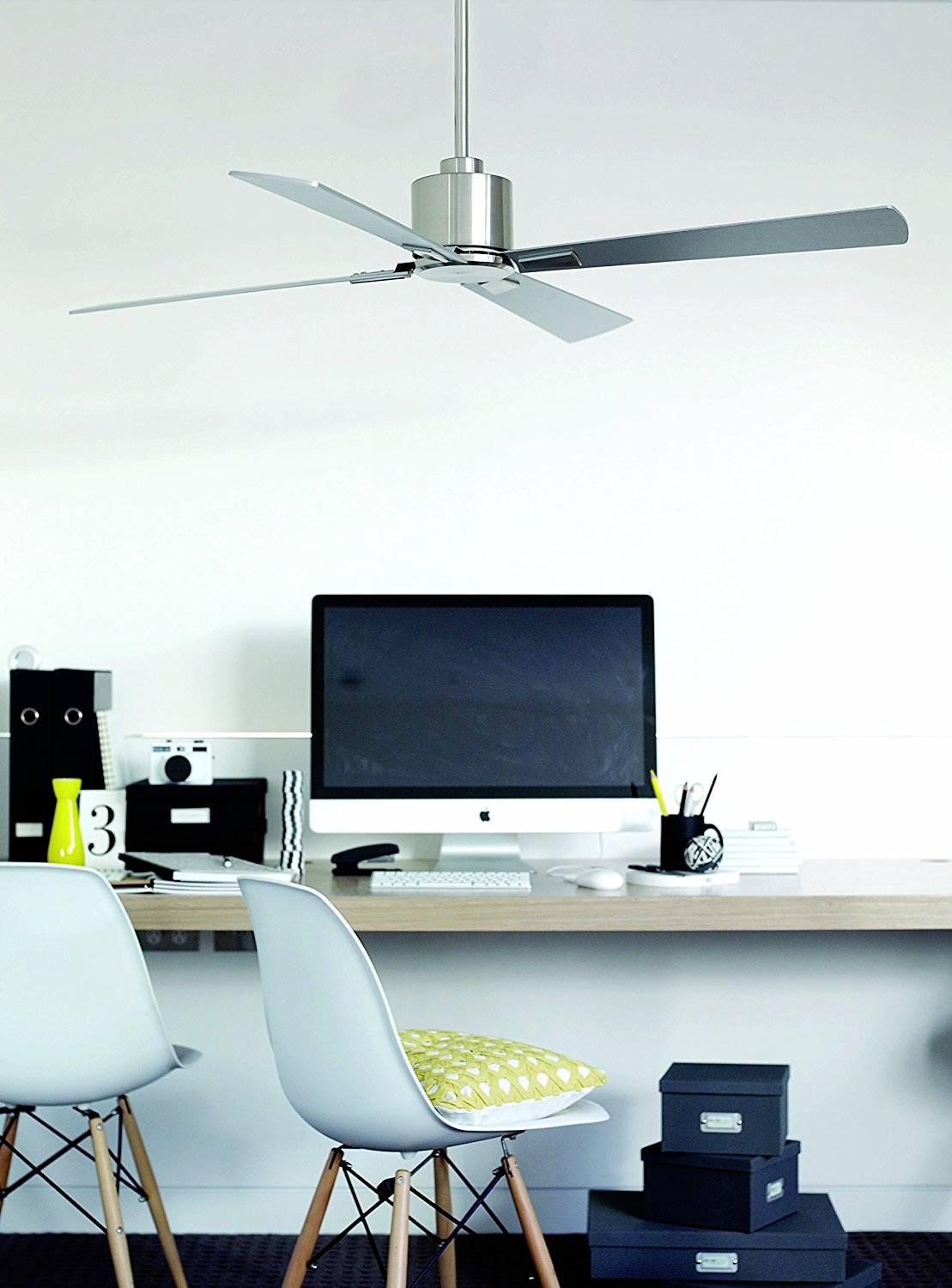 Moderner Arbeitsplatz mit Computer auf einem Holzschreibtisch, zwei weißen Stühlen mit gelbem Kissen, schwarzes Regal und Deckenventilator.