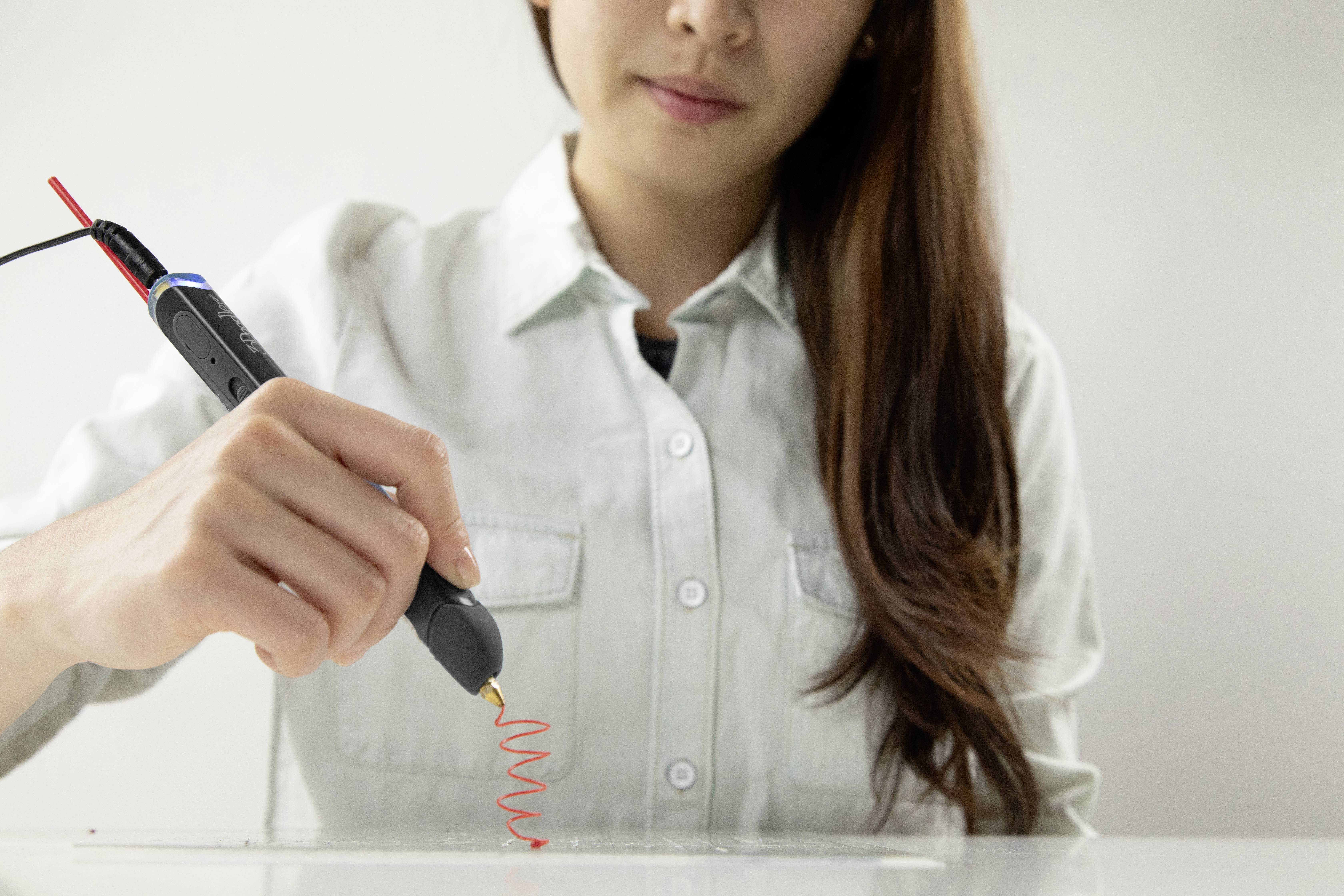 Eine Frau benutzt einen 3D-Stift, um rote, spiralförmige Linien auf einer Tischoberfläche zu zeichnen.