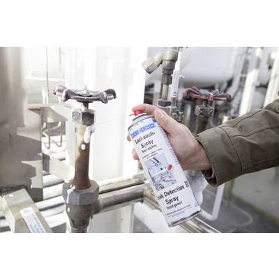 Person hält eine Dose Lecksuchspray und sprüht es auf ein Rohrventil in einer technischen Umgebung, um Lecks zu prüfen.