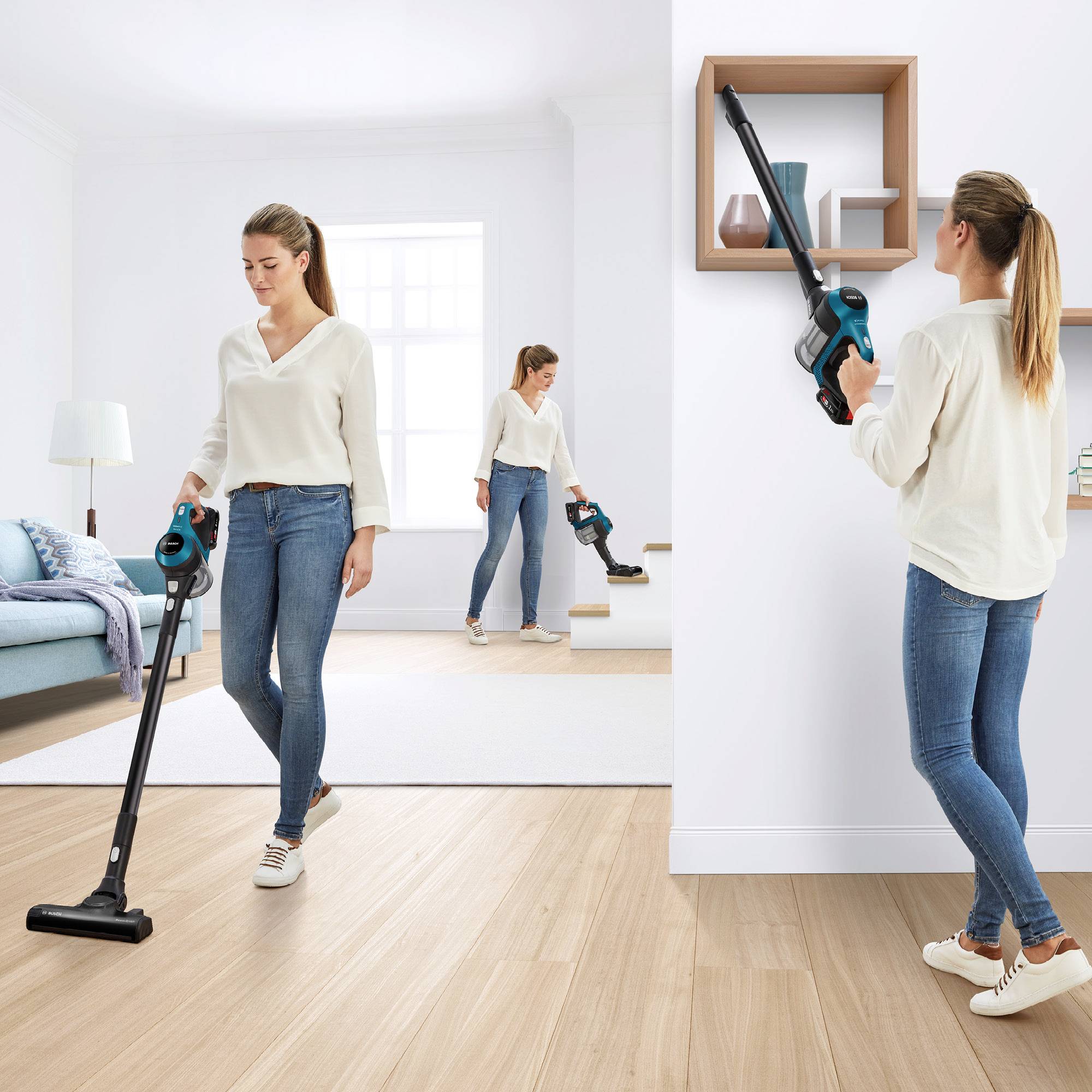 Eine Frau benutzt einen kabellosen Staubsauger im Wohnzimmer, zeigt verschiedene Reinigungspositionen. Im Hintergrund Sofa und weißes Regal.