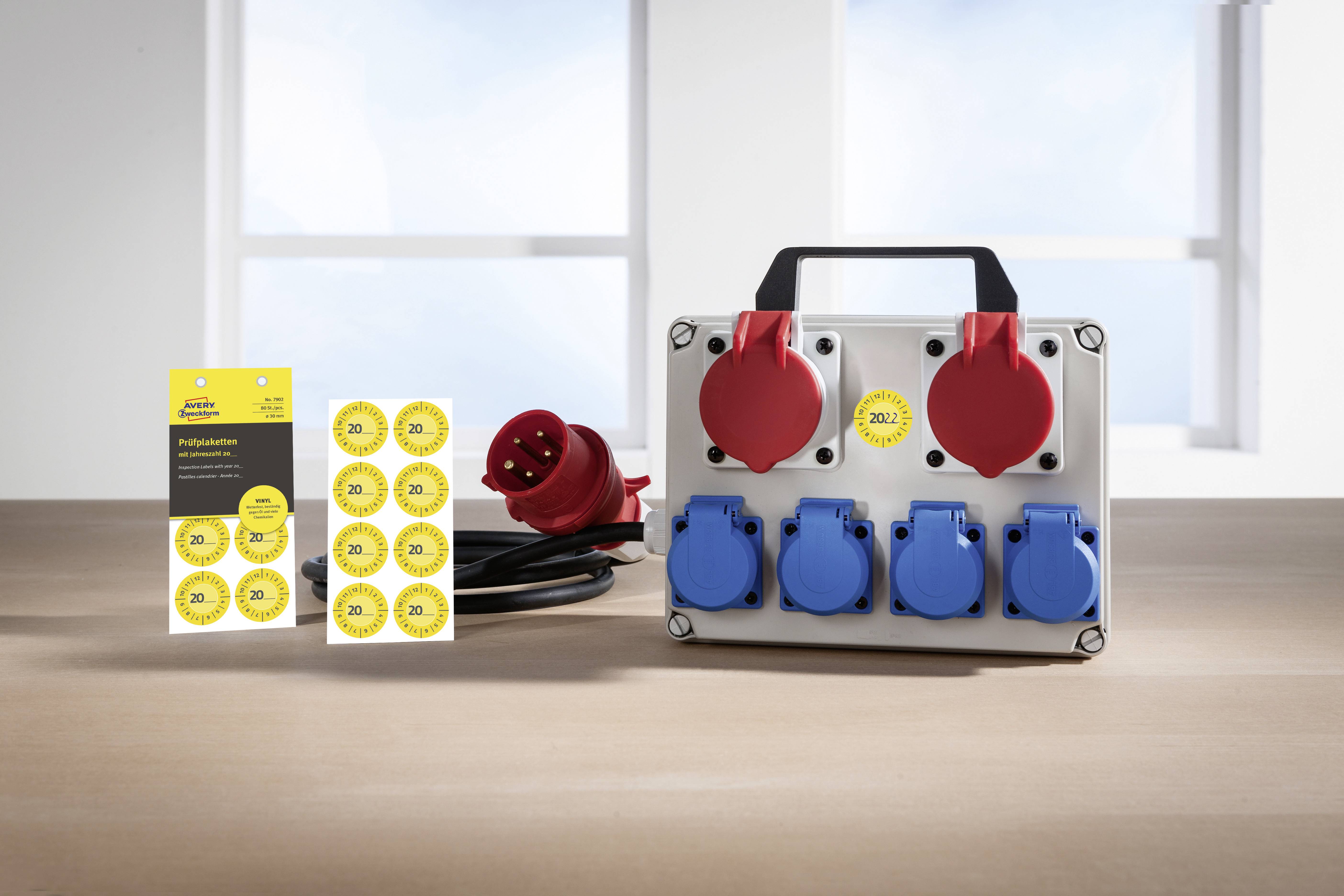 Industrie-Steckdosenbox mit mehreren roten und blauen Steckdosen, daneben Aufkleber mit Prüfplaketten zur elektrischen Sicherheit.