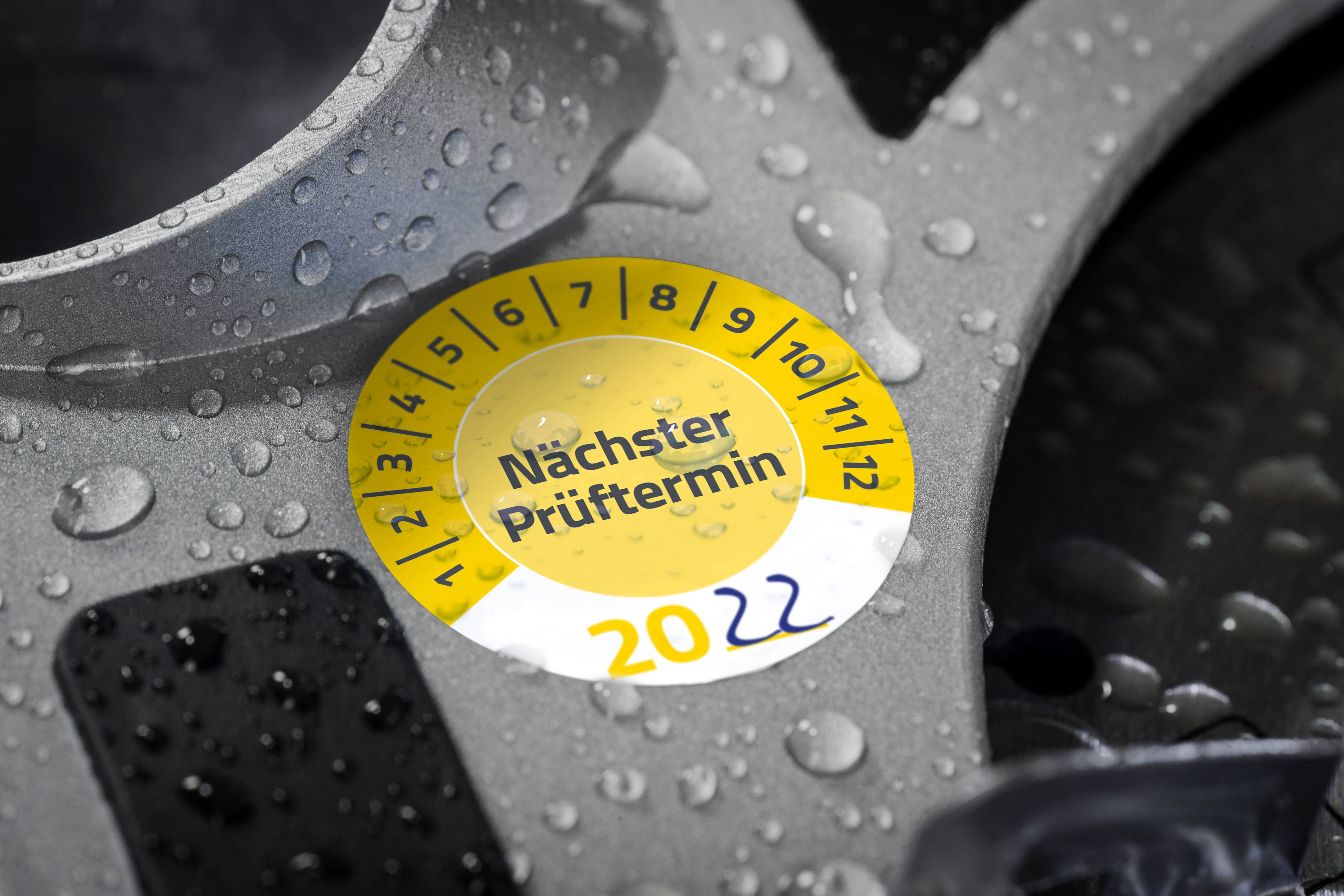 Ein gelber Prüfsiegel-Aufkleber auf einem silbernen Autoteil zeigt den nächsten Prüftermin: Oktober 2022.