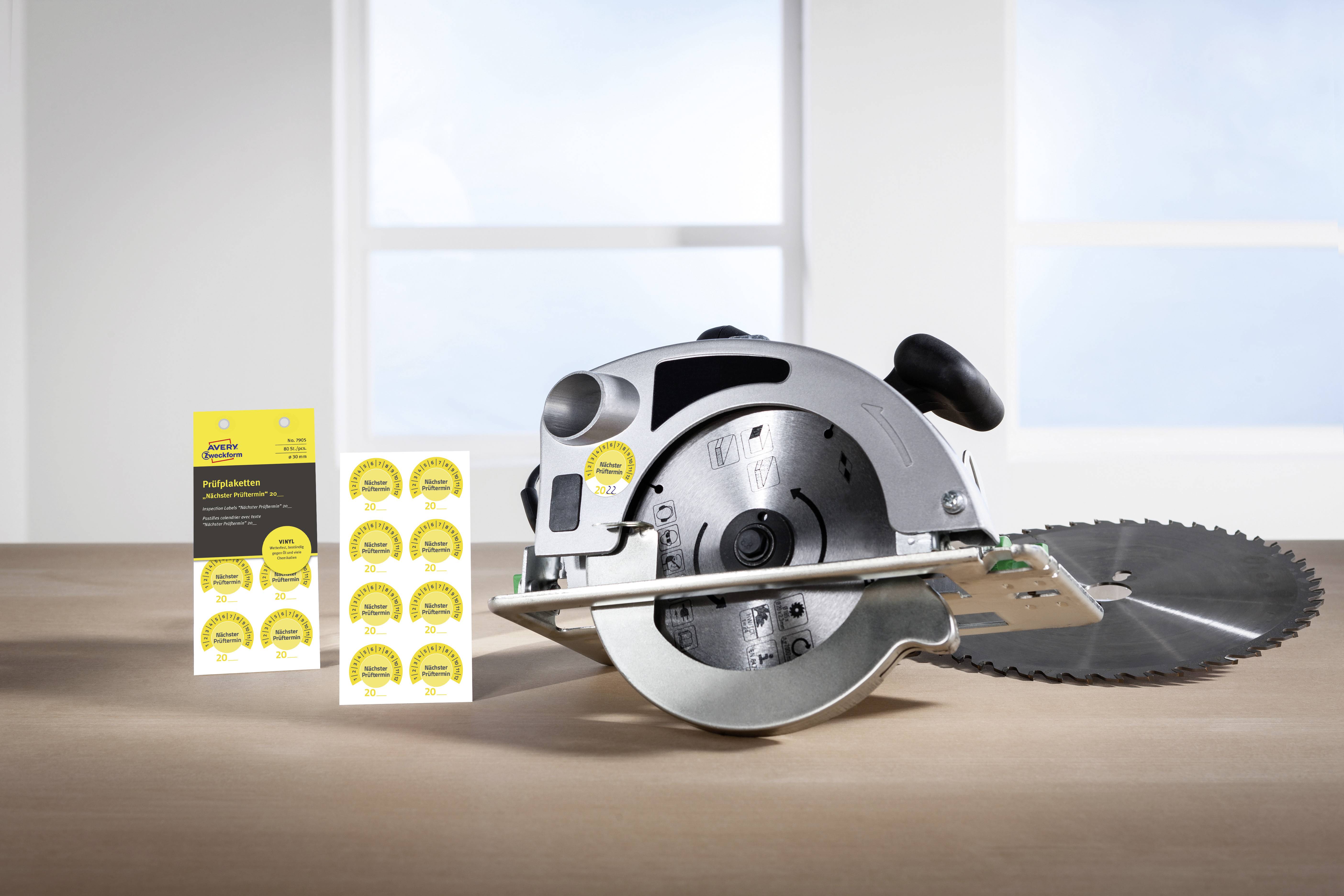 Elektrische Kreissäge auf einem Holztisch, flankiert von Aufklebern mit Text und Grafiken. Fenster im Hintergrund.