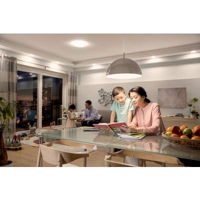 Eine Familie sitzt im Wohnzimmer. Eine Frau liest einem Jungen ein Buch vor. Im Hintergrund spielen ein Mann und ein Mädchen.