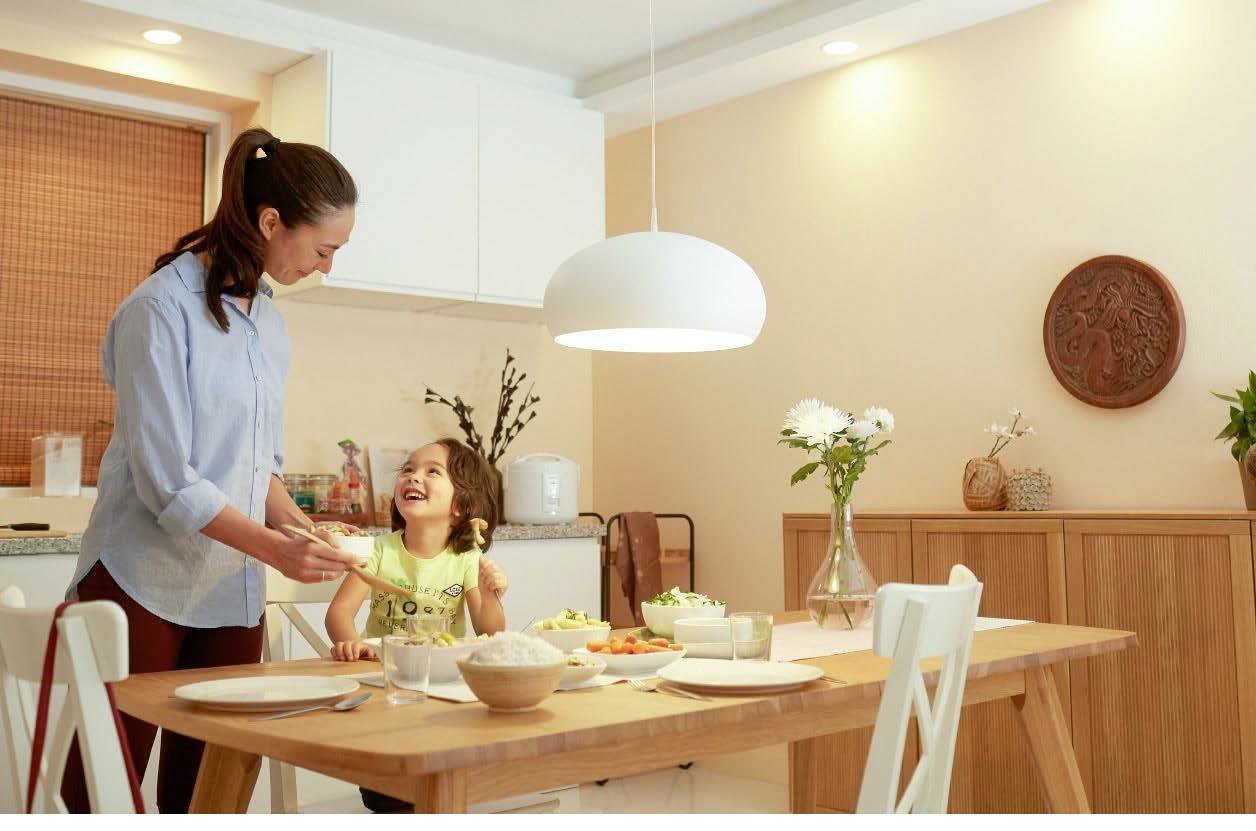 Eine Frau und Kind lachen in einer modernen Küche beim gemeinsamen Essen. Der Tisch ist mit Geschirr und Speisen gedeckt.