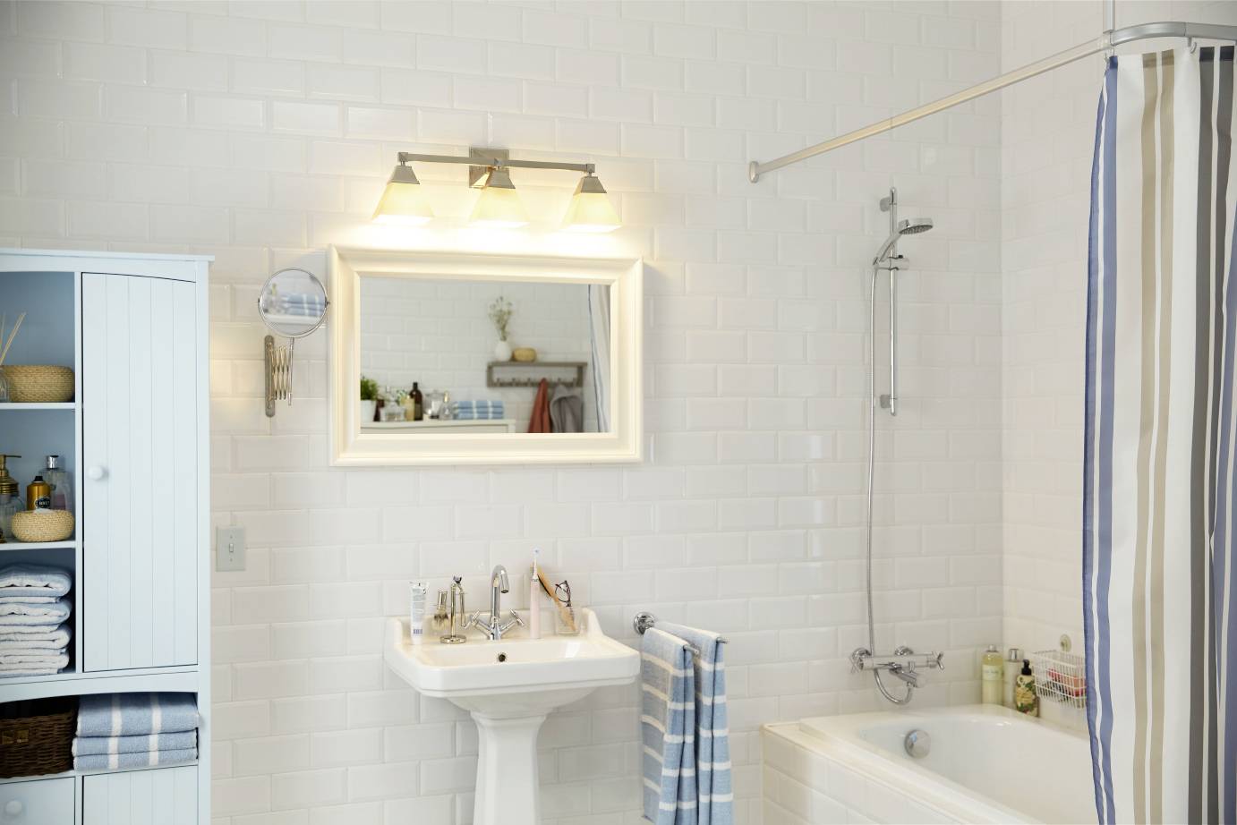 Helles Badezimmer mit weiß gefliesten Wänden, Badewanne, Duschvorhang und Waschbecken. Schrank mit Handtüchern links.