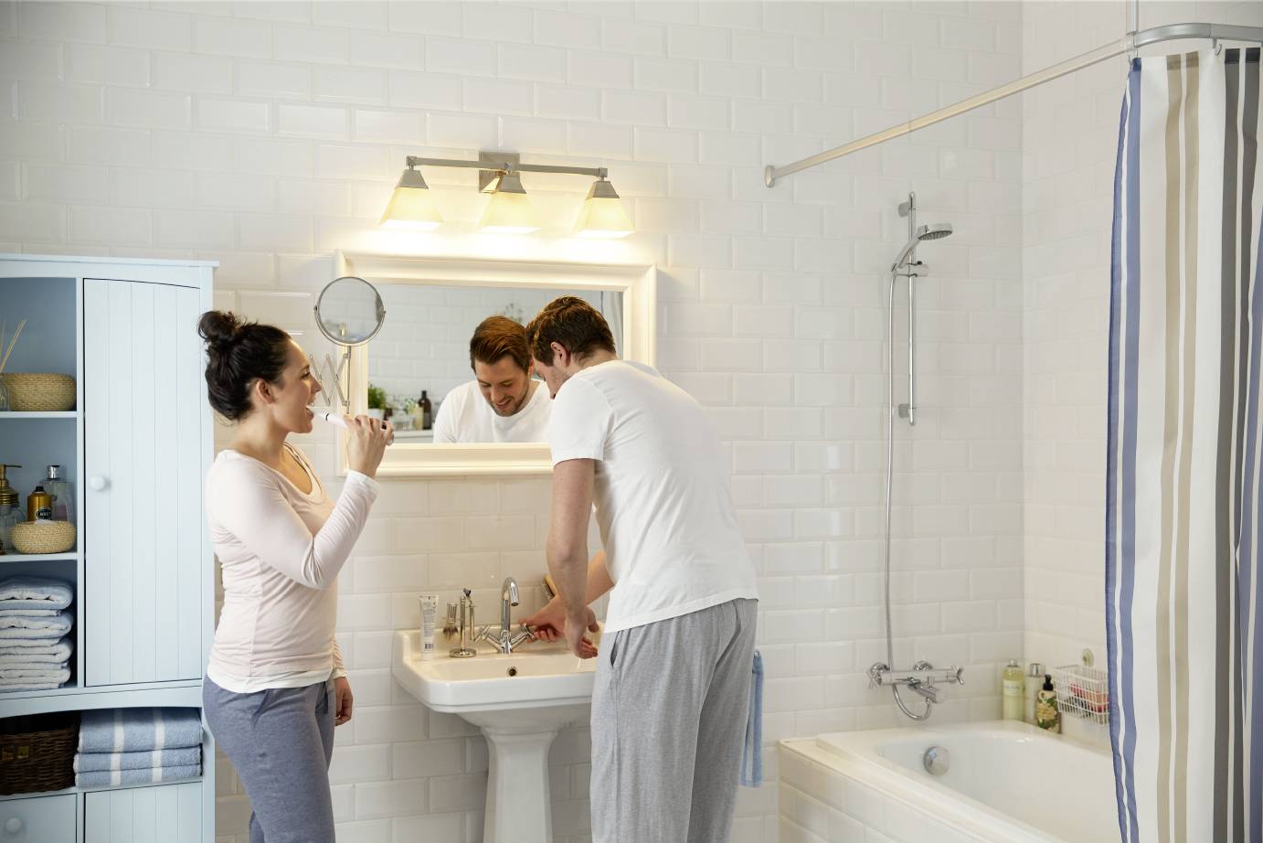 Eine Frau und ein Mann im gemütlichen Badezimmer beim Zähneputzen. Sie lachen miteinander vor einem Spiegel über dem Waschbecken.