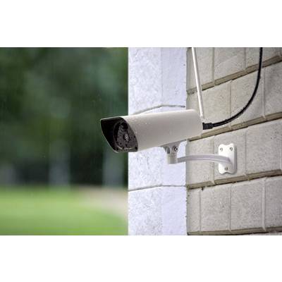 Überwachungskamera an einer Hauswand, gerichtet auf einen grünen Außenbereich, überwacht Sicherheit des Anwesens.