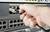 Eine Hand steckt ein Kabel in einen Netzwerk-Switch, was auf eine Netzwerkverbindung oder -einrichtung hindeutet.