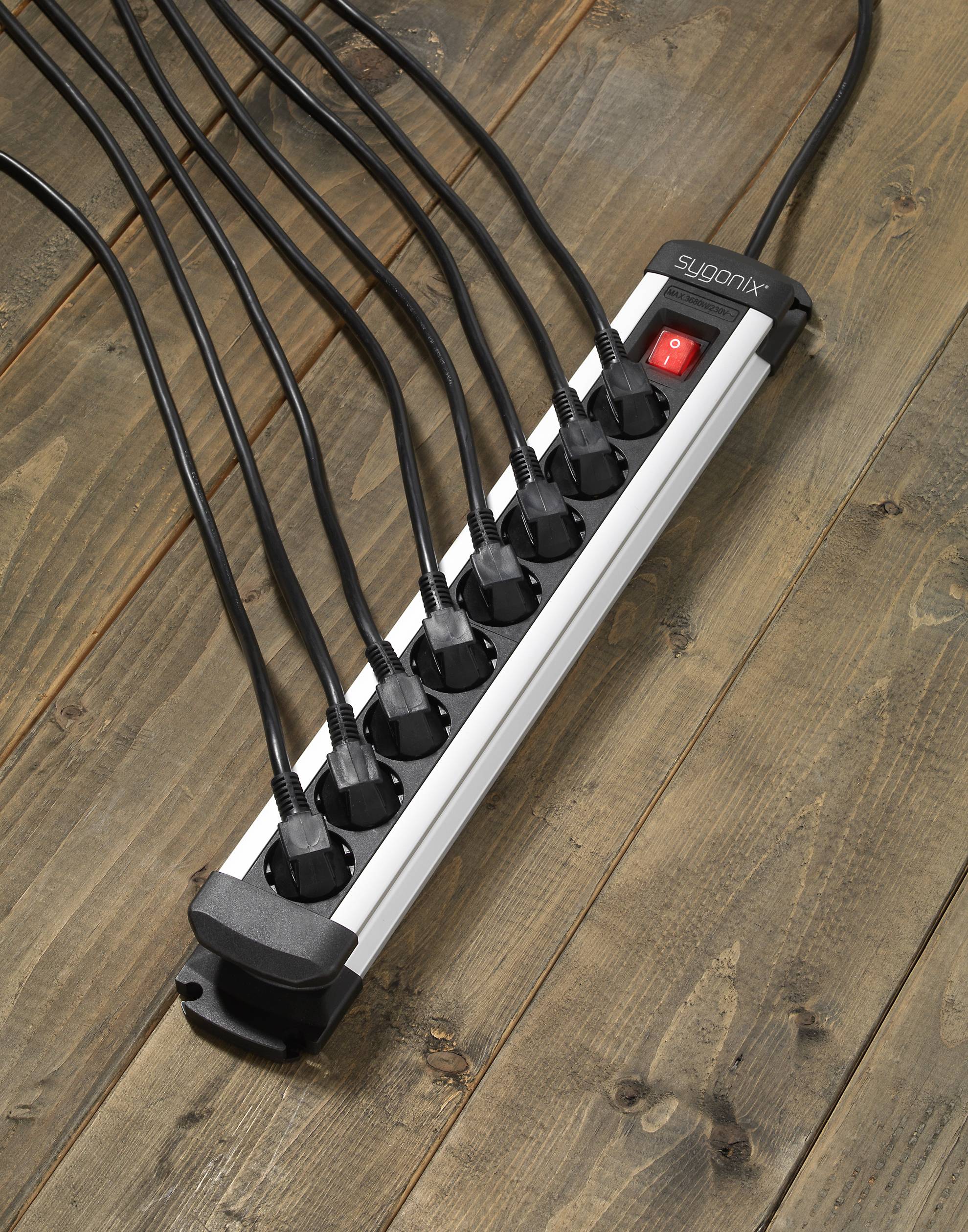 Eine mit acht angeschlossenen schwarzen Steckern befüllte Steckdosenleiste liegt auf einem Holzboden. Ein roter Schalter ist eingeschaltet.