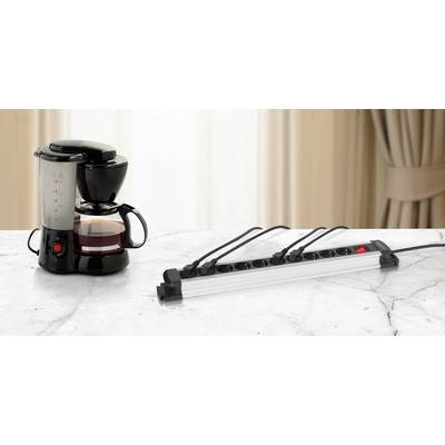 Kaffeemaschine auf Marmortisch, neben einer eingeschalteten Mehrfachsteckdose mit mehreren angeschlossenen Kabeln.