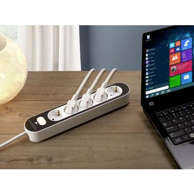 Mehrfachsteckdose mit drei eingesteckten Kabeln neben einem Laptop auf einem Holztisch; ein sanft beleuchtetes Licht im Hintergrund.
