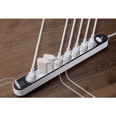 Mehrfachsteckdose mit neun Steckplätzen, in denen mehrere weiße Kabel und Adapter eingesteckt sind. Liegt auf einem Holztisch.