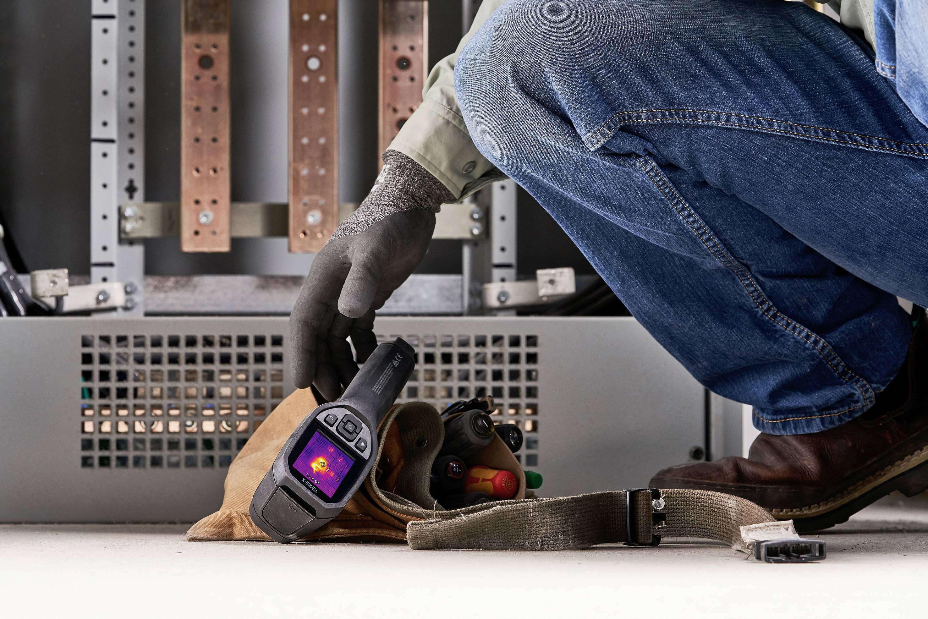 Eine Person hält ein Wärmebildkamera-Gerät vor einem elektrischen Schaltschrank, um Temperaturunterschiede zu überprüfen.