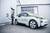 Ein Mann lädt ein Elektroauto vor einem Industriegebäude auf. Das Auto ist weiß mit grünen Akzenten und trägt das Logo 'els speisberg'.