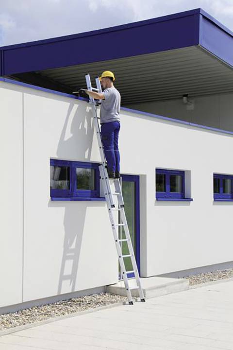 Eine Person auf einer Leiter arbeitet an einem Flachdach eines Gebäudes. Sie trägt einen gelben Schutzhelm.