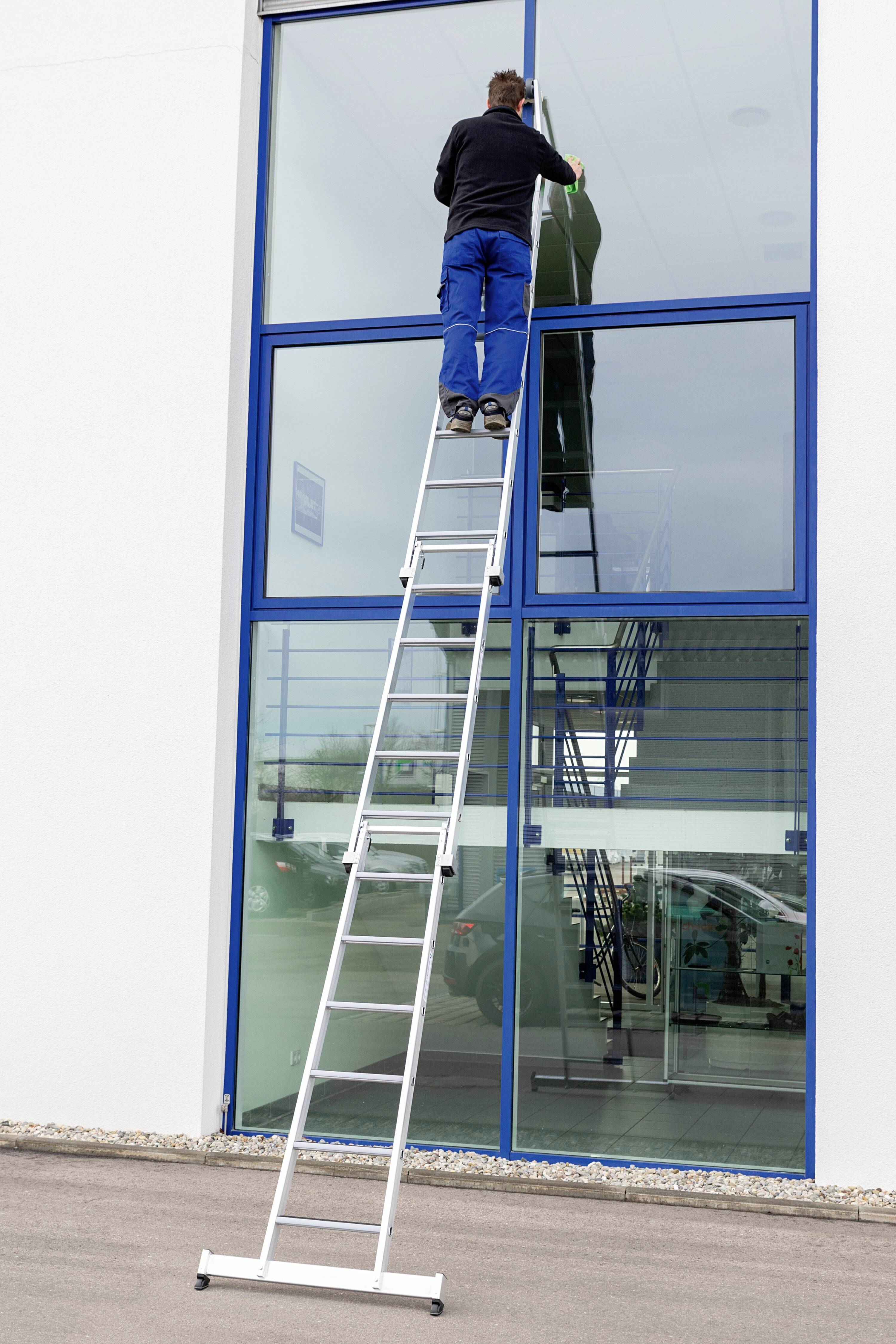 Person auf Leiter reinigt große Fenster an Gebäude.