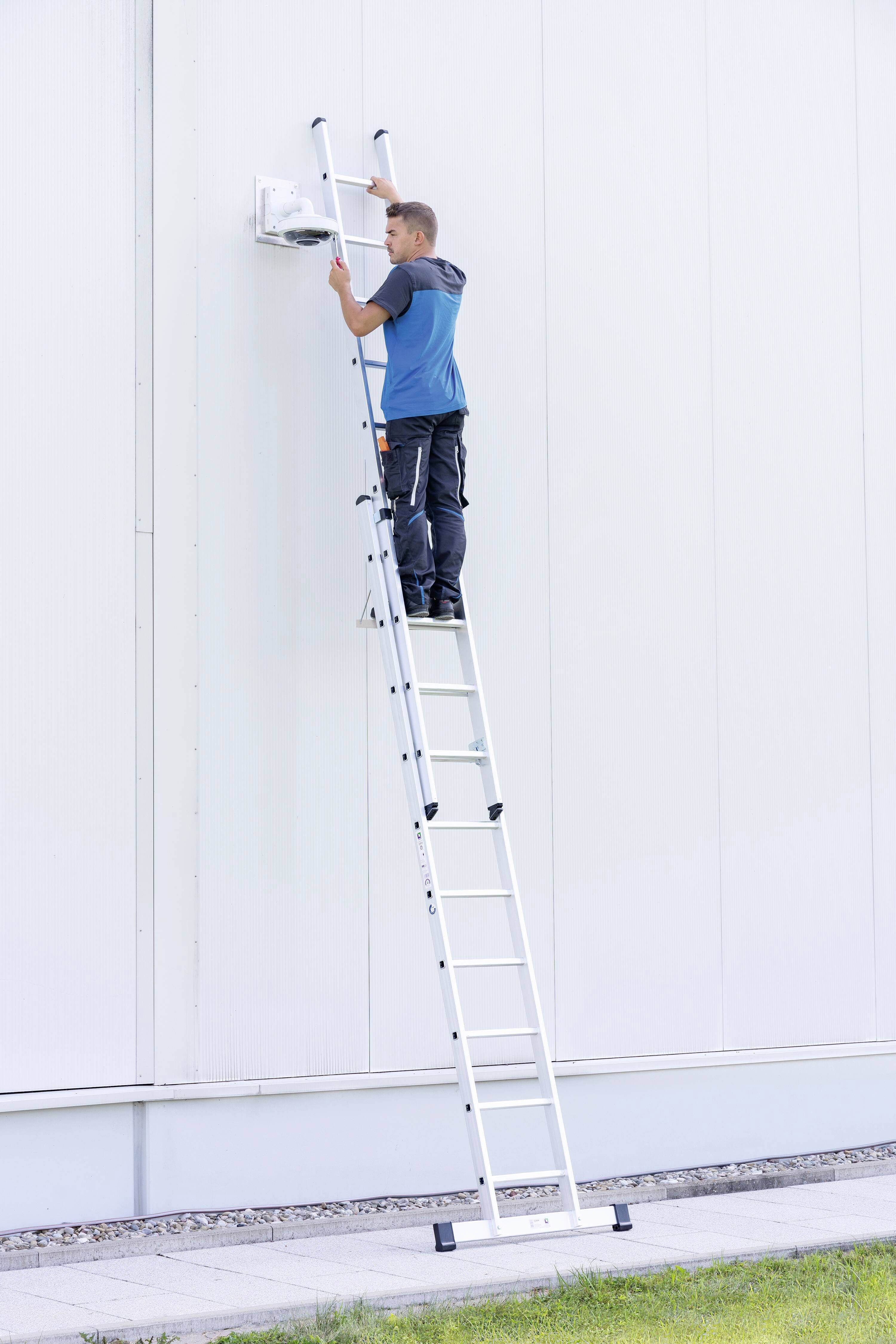 Eine Person steht auf einer Leiter und arbeitet an einer Wandinstallation an einem hohen Gebäude.