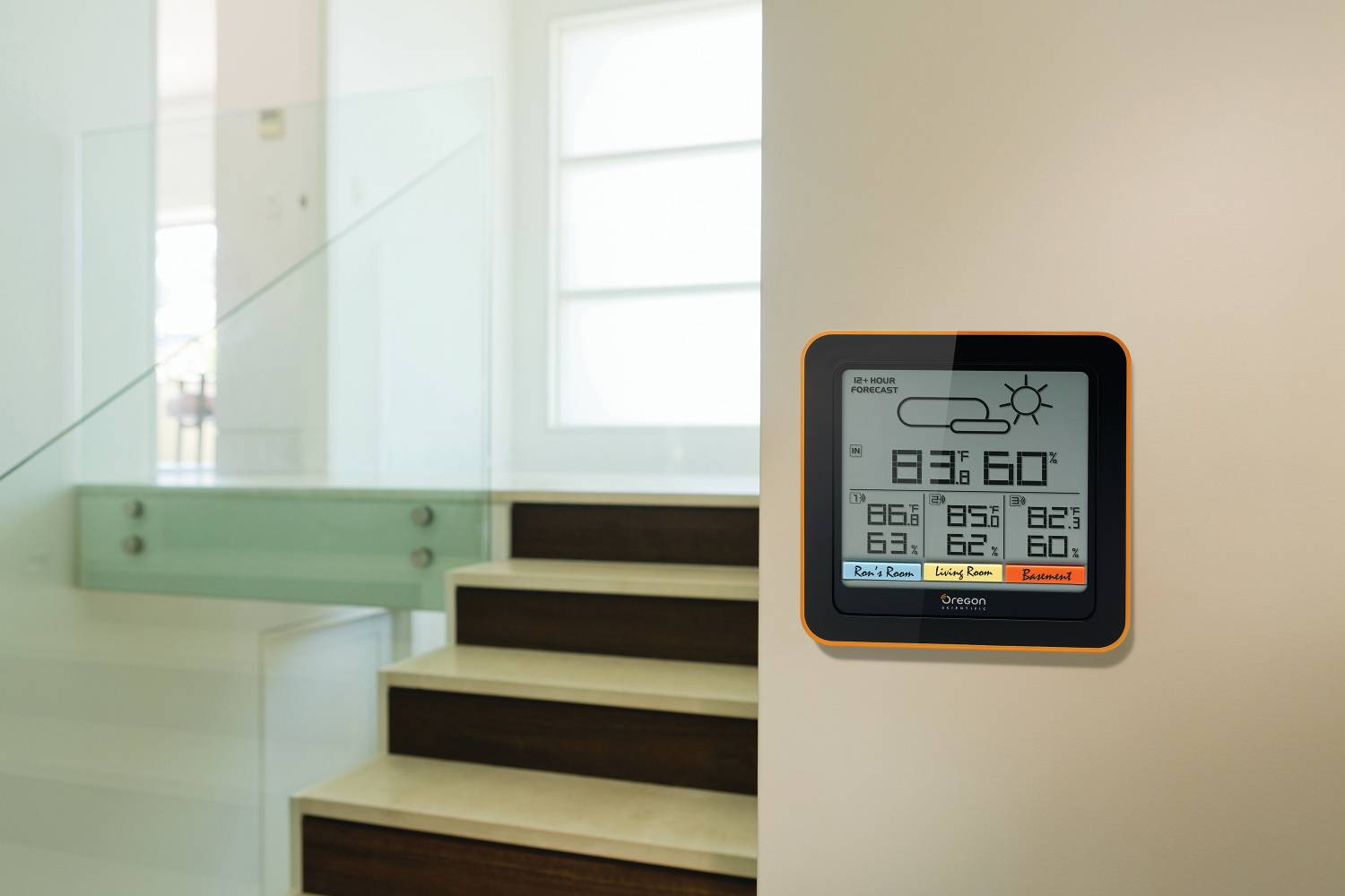 'Intelligentes Thermostat an der Wand zeigt 83 % Luftfeuchtigkeit und 60°F an. Helle, moderne Umgebung mit Treppe im Hintergrund.'