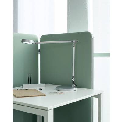 Ein moderner Schreibtisch mit grüner Trennwand, silberner Schreibtischlampe, Stiften, Notizblock und Visitenkarten auf dem weißen Tisch.