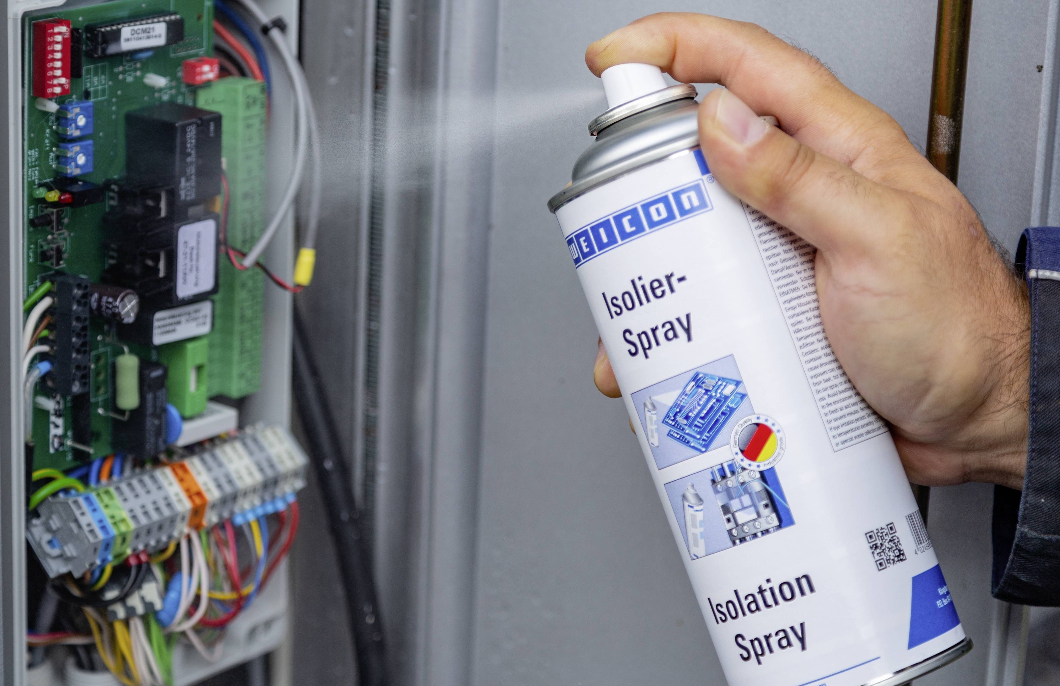 Eine Person sprüht Isolierspray auf einen offenen elektrischen Schaltkreis, um ihn zu schützen, mit sichtbaren Kabeln und Komponenten.